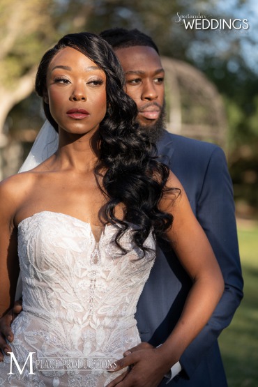stunning photo of African American bride with long curls swept over her shoulder and a beautiful strapless wedding gown from celebrations bridal. Her groom dresed in a cobalt suit gazes over her shoulder.