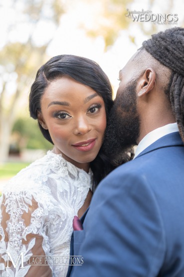 Bride looks happily at the camera while her groom whispers in her ear. Lovely African American couple in white an cobalt.